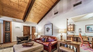 A cozy living room with a wooden ceiling, leather sofa, and a dining area with wooden furniture. - Timbers Lodge | Your Ruidoso Retreat w/ Hot Tub Bliss, Wildlife Views & Cozy Comforts (Ruidoso)