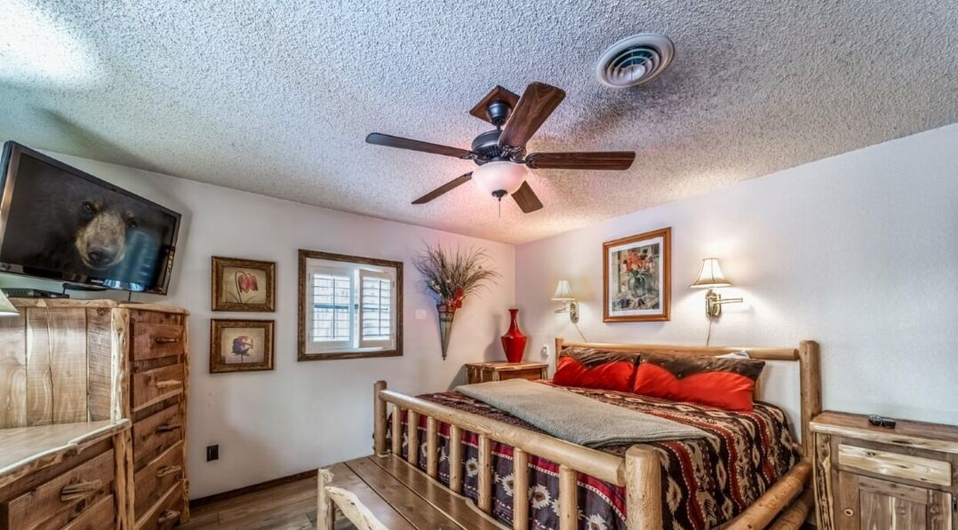 A bedroom with a wooden bed, a ceiling fan, a TV, and a window.