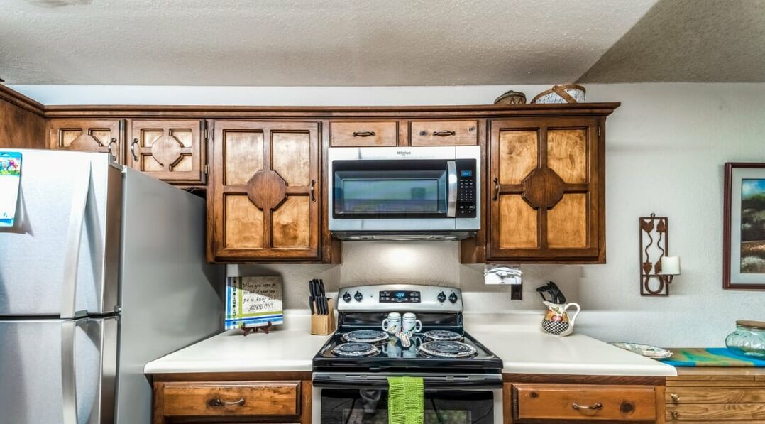 A kitchen with wooden cabinets, a stainless steel refrigerator, a microwave, and a stove.