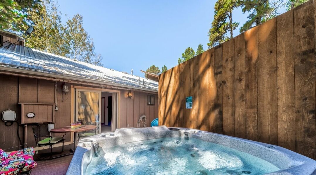 A hot tub in a backyard with a wooden fence, a patio table, and a chair.