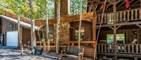 A rustic cabin with a wooden deck, a bench, and a stone wall.