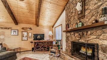 Interior acogedor de una cabaña con chimenea de piedra, vigas de madera en el techo y un televisor.