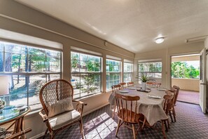 Un comedor con una mesa grande, sillas y vistas a un jardín a través de amplias ventanas.