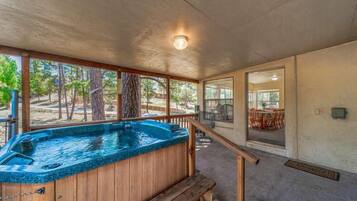 A hot tub with a wooden deck, a covered outdoor area, and a view of the outdoors.
