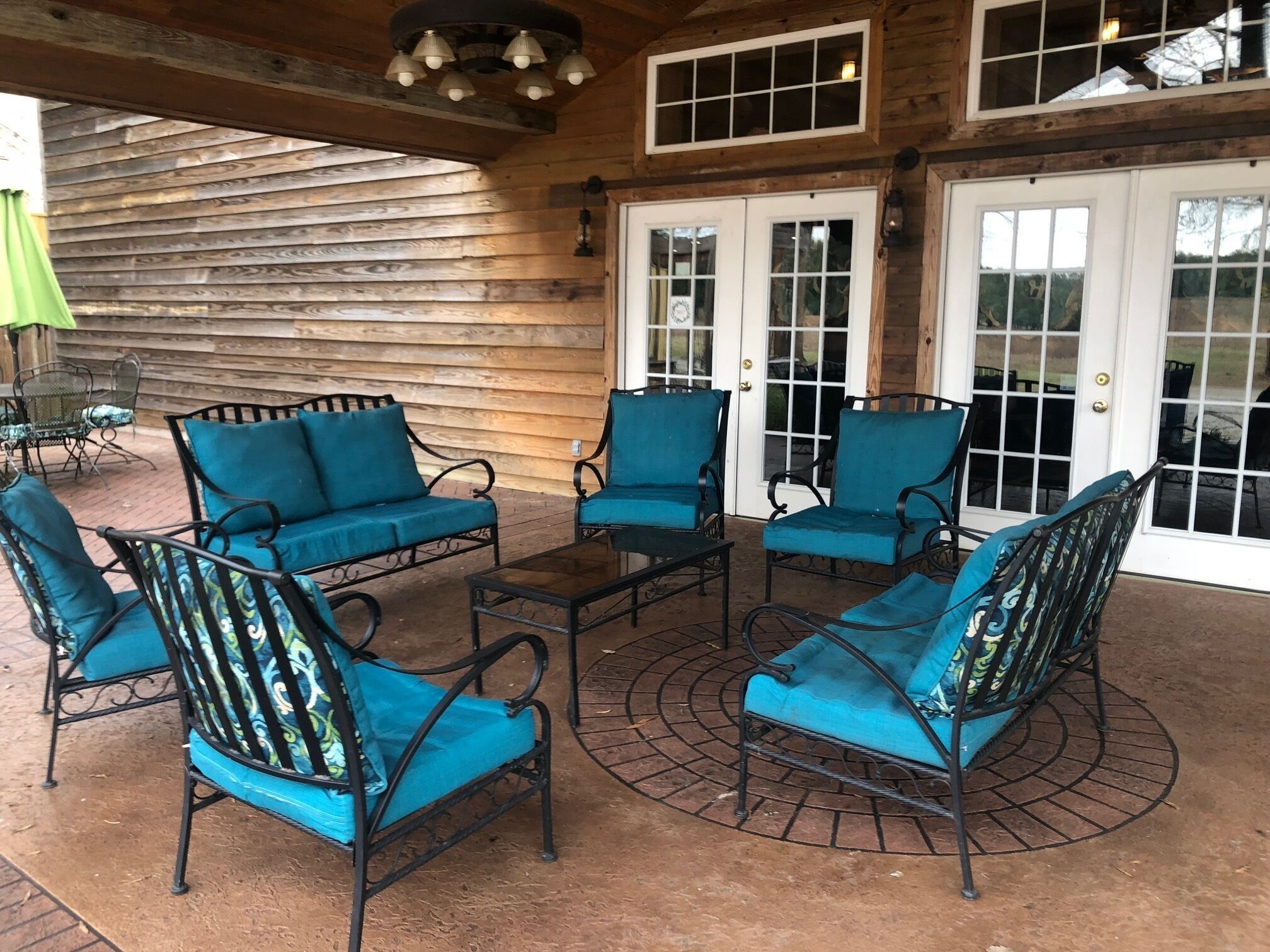 Ein überdachter Patio-Bereich mit vier blauen, gepolsterten Stühlen und einem kleinen Tisch, Holzverkleidung und einem großen Fenster mit Blick ins Freie.
