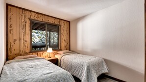 Una stanza con due letti, pareti in legno, una finestra vista alberi e un comodino con una lampada.