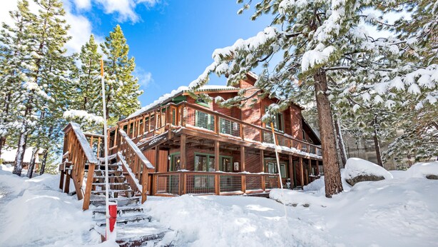 Una baita di legno con una scala che conduce a un patio, circondata da alberi innevati.