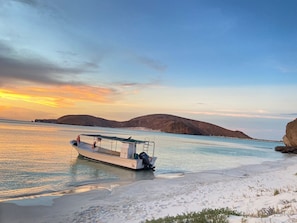 A boat docked at a sandy beach with calm water and distant hills.