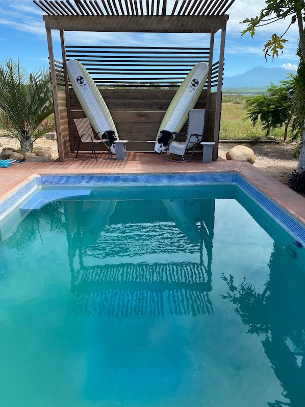 A swimming pool with two lounge chairs and a wooden pergola structure.
