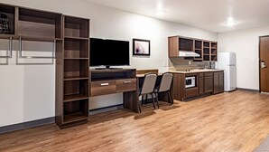 A modern kitchen with a built-in TV, wooden cabinets, and a dining area with chairs. - WoodSpring Suites Toledo Maumee (Maumee)