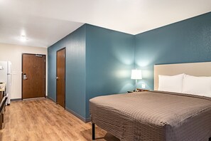 A bedroom with a bed, a nightstand, a lamp, and a door. - WoodSpring Suites Toledo Maumee (Maumee)