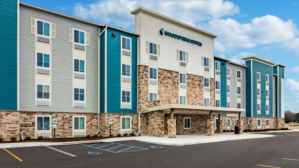 A multi-story hotel with a stone facade and blue accents, featuring a covered entrance and handicap-accessible parking. - WoodSpring Suites Toledo Maumee (Maumee)