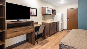 A compact room with a bed, a desk with a TV, a kitchenette, and a door. - WoodSpring Suites Toledo Maumee (Maumee)