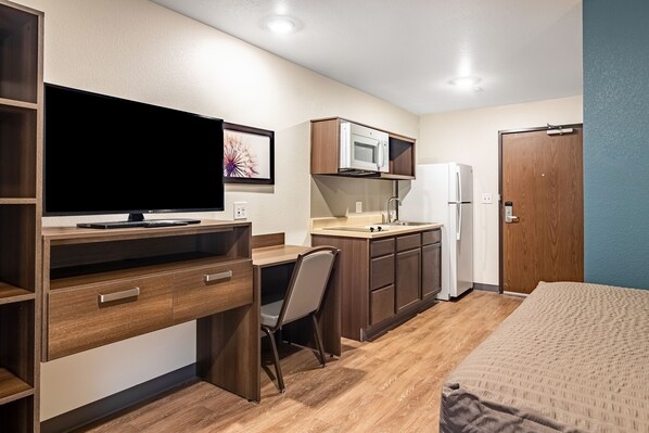 A compact room with a bed, a desk with a TV, a kitchenette, and a door. - WoodSpring Suites Toledo Maumee (Maumee)