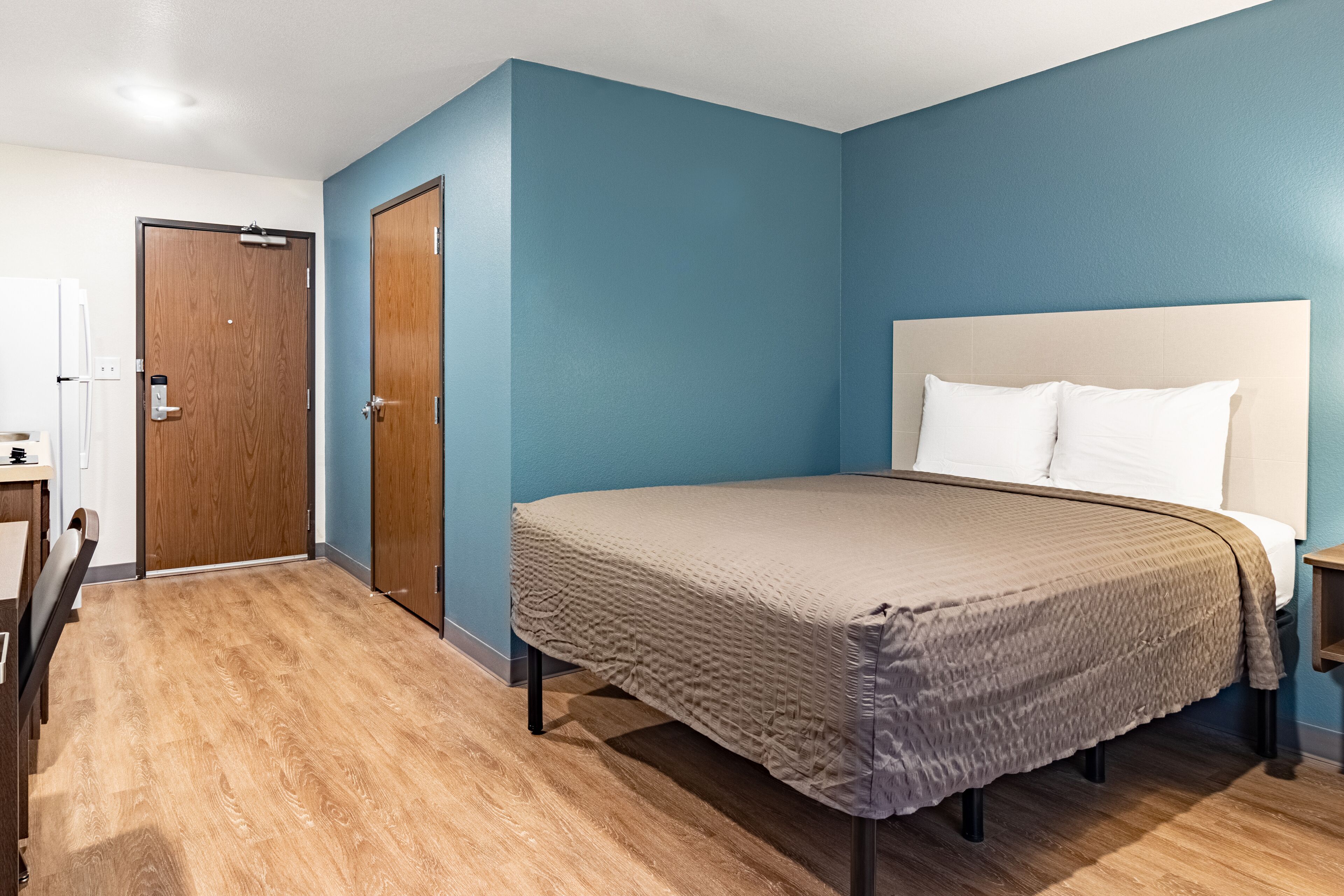 Een slaapkamer met een bed, houten vloer en een deur.