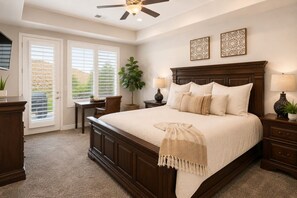 A bedroom with a large bed, a desk, a chair, a ceiling fan, and two wall-mounted decorative items.