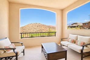 A balcony with a view of a hilly landscape, a wooden table, and two sofas with cushions.