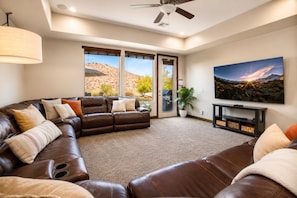 A living room with a sectional sofa, a flat-screen TV, and a large window with a desert view.