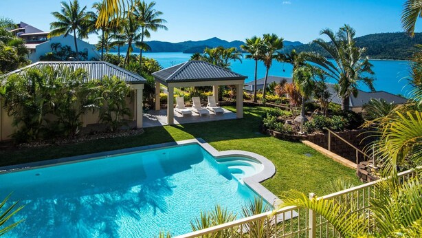A swimming pool with a gazebo, palm trees, and a view of the sea.