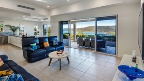 A modern living room with a blue sofa, a coffee table, and a view of a lake through large sliding doors.