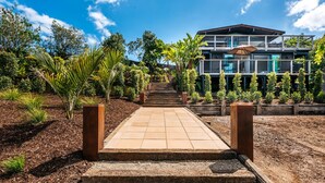 Una casa de varios niveles con un camino empedrado que lleva a la entrada, rodeada de plantas y árboles.