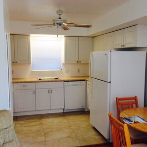 Compact kitchen with a refrigerator, dining table, and ceiling fan.