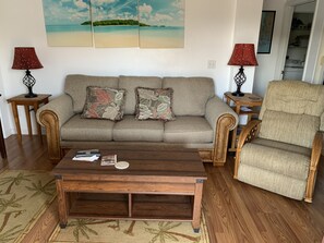 Relax in this inviting living room with a comfortable sofa, wicker armchair, and a beautiful landscape painting.