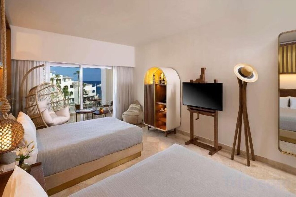 A hotel room with two beds, a television, a lamp, and a view of the city.