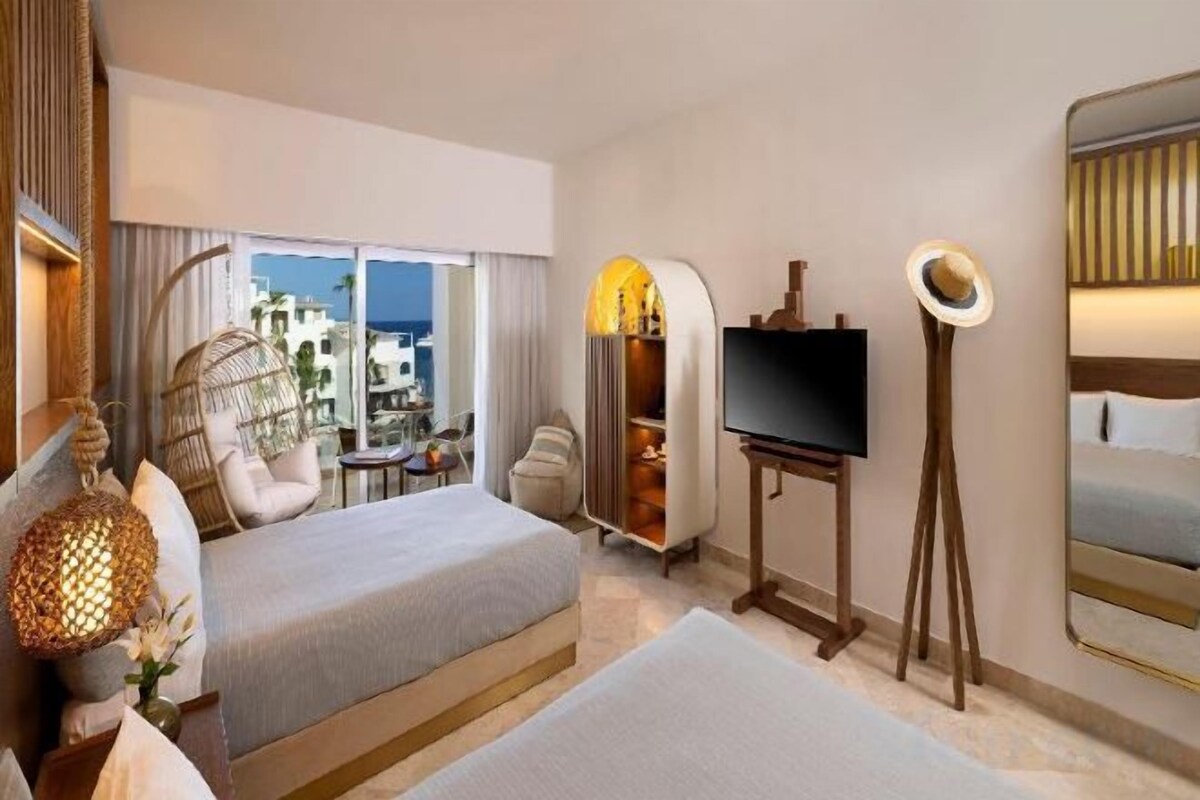 A hotel room with a bed, a TV, a balcony with a view, and a large mirror.