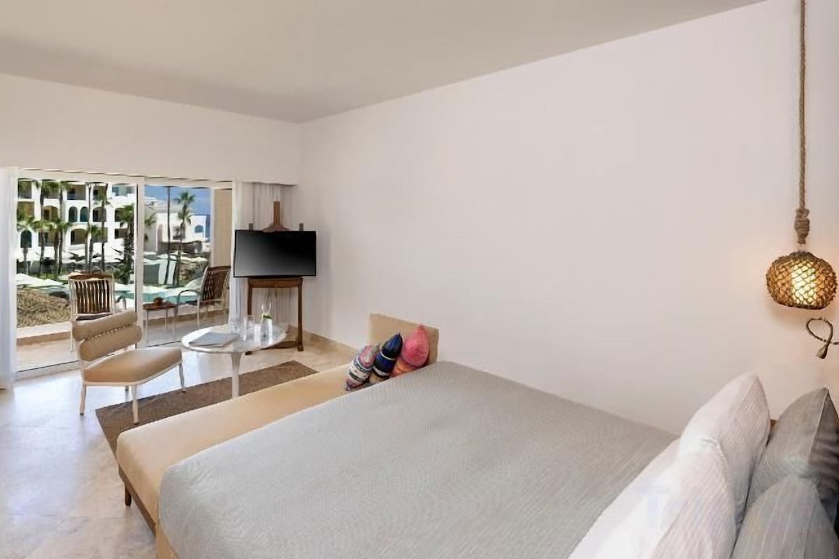 A hotel room with a bed, a TV, a seating area with a table, and a view of the outdoor area.