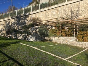 A stone wall with a metal railing, a grassy area, and a pergola structure.