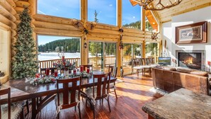 L’intérieur d’une cabane en rondins comprend un coin repas, une cheminée et de grandes fenêtres donnant sur une zone boisée.