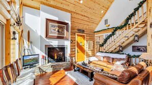 L’intérieur d’une cabane en rondins, avec une cheminée, des murs en bois, un canapé et un escalier décoré de guirlandes.