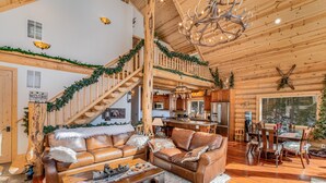 L’intérieur chaleureux d’un chalet en bois, avec un escalier en bois, des canapés en cuir, un coin repas et un lustre.