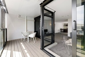 A modern apartment with a balcony, a dining area with white chairs, and a kitchen visible through an open door. - Central Apartment with Pool, Spa, Sauna and Gym (Mount Maunganui)