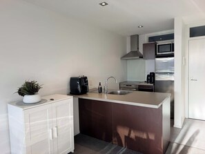 A modern kitchen with a central island, stainless steel appliances, and a white cabinetry design. - Central Apartment with Pool, Spa, Sauna and Gym (Mount Maunganui)