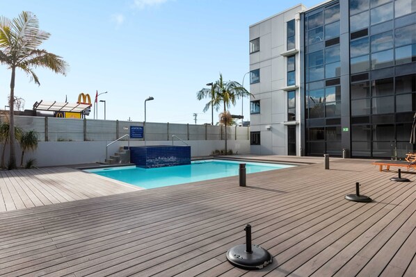 Un edificio moderno con piscina, terraza de madera y palmeras.
