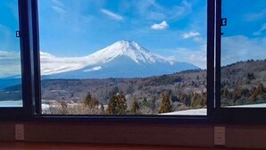 A window view of a snow-capped mountain, likely a volcano, with a forested valley below. - Rokumeikan HILLS (Yamanakako)