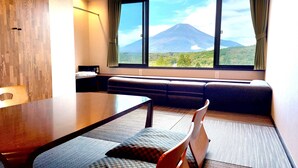 A room with a wooden floor, a dining table, a sofa, and a large window with a mountain view. - Rokumeikan HILLS (Yamanakako)