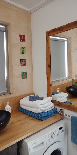 A laundry area with a washing machine, stacked towels, a mirror, and a window. - Gingko Lodge. Country luxury with a view. (Mossiface)
