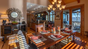 A spacious dining area with a wooden table set for a meal, a chandelier, and a view of the kitchen and outdoor deck. - B Rock Ridge at Echota - townhome with private hot tub! (Banner Elk)