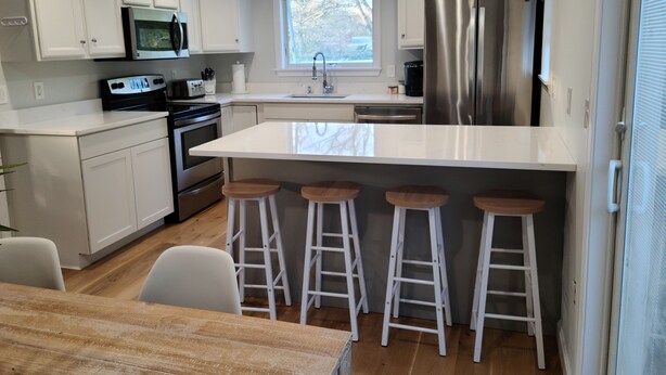 Een moderne keuken met witte kasten, roestvrijstalen apparatuur en een centraal eiland met barkrukken.