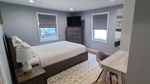 Een slaapkamer met een bed, nachtlampje, dressoir en een bureau met stoel.