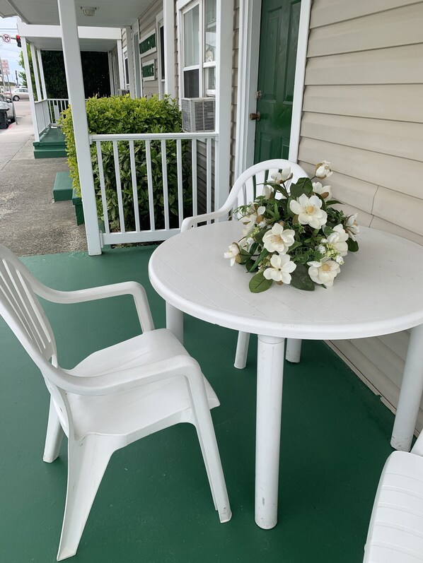 A white plastic table and chairs on a green outdoor patio with a white railing and a white door.