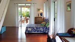 A bedroom with a bed, a desk, and a chair. There is a staircase on the left and a door leading to a balcony. - Villa Iris by Tahiti Homes  (Moorea-Maiao)