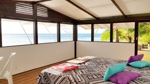 A room with a bed, a view of the sea, and a palm tree outside. - Villa Iris by Tahiti Homes  (Moorea-Maiao)