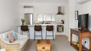 Un espace de vie compact comprenant un coin cuisine, un canapé avec des coussins, une table basse et un téléviseur posé sur un meuble en bois.