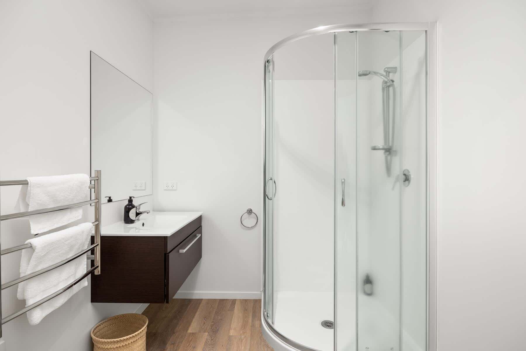 Une salle de bain moderne avec une douche à l’italienne en verre, un lavabo blanc et un meuble en bois foncé.