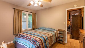 Une chambre à coucher avec un lit, un ventilateur de plafond, une fenêtre avec des rideaux, une commode en bois et un mur en briques.