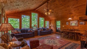 L’intérieur chaleureux d’un chalet avec un grand plafond en bois, deux canapés ornés de coussins à motifs, une table à manger avec des chaises et un tapis aux motifs géométriques.